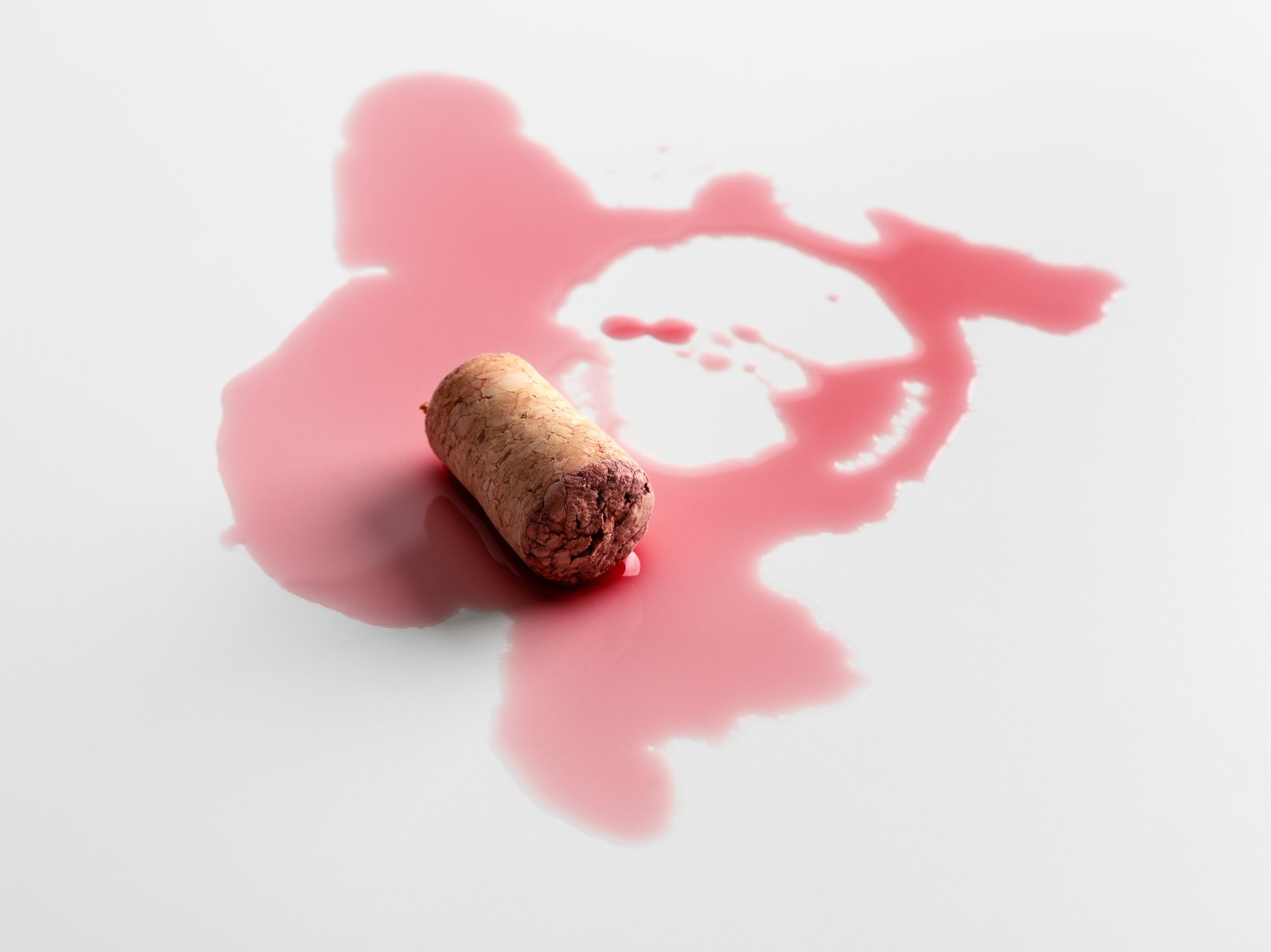 Red wine cork with spilled liquid creating abstract stain on light background. Concept of accident, imperfection and symbolic elegance in minimalistic composition.