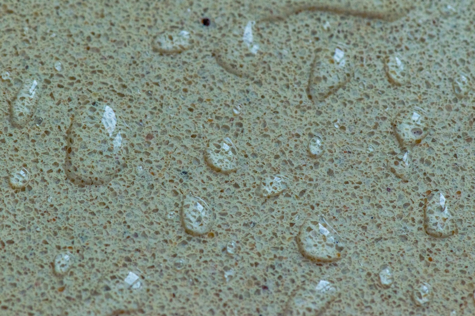 Macro photograph showing water droplets on a porous beige stone surface, demonstrating waterproof and moisture-resistant properties
