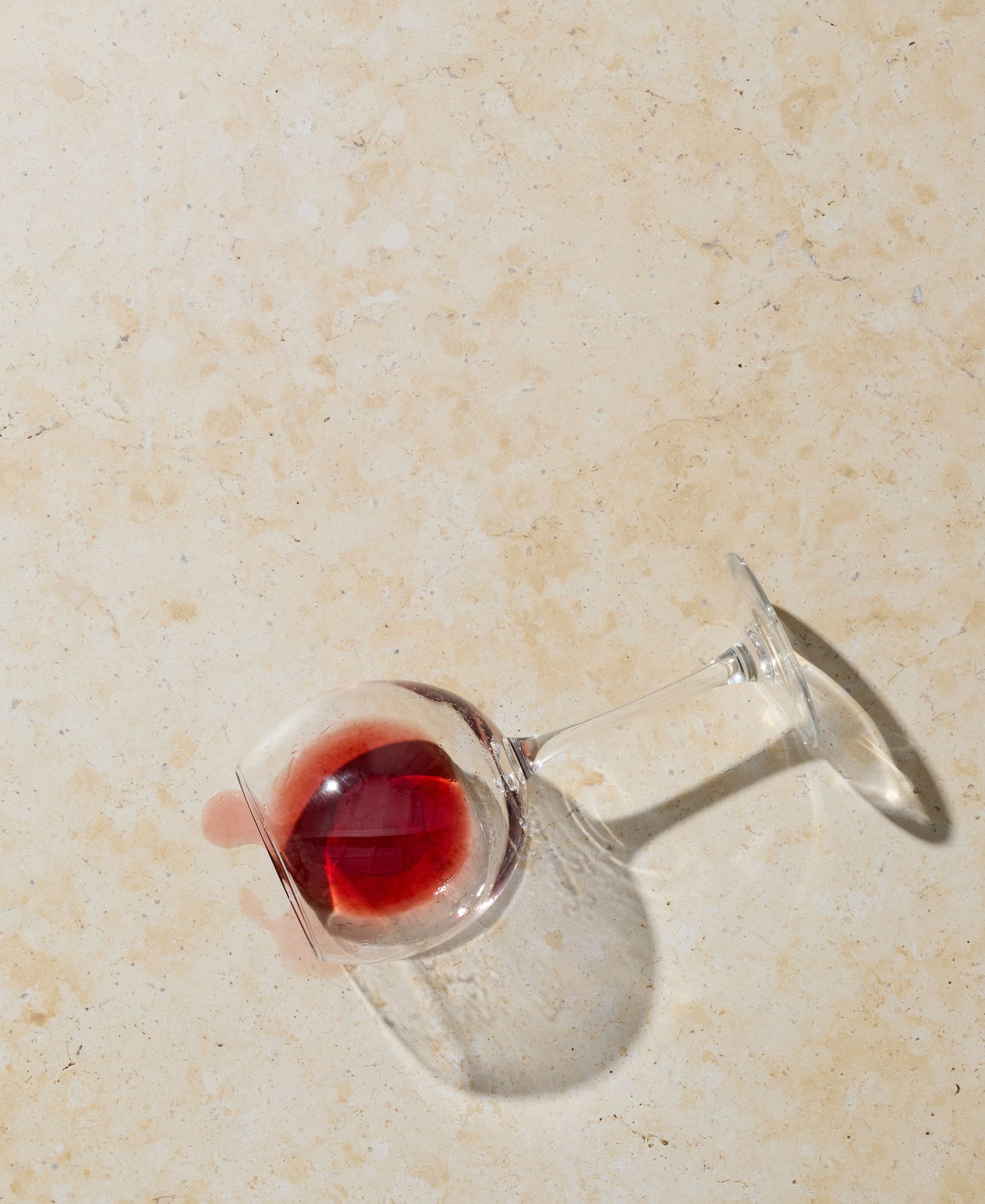 Top view of a fallen wine glass with red wine spilled on a light stone surface